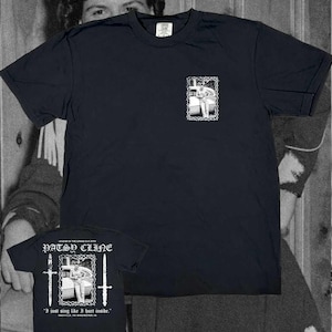 Peut inclure: Un t-shirt noir à manches courtes avec un petit motif blanc sur la poitrine et un grand motif au dos. Le design arrière comprend un portrait de Patsy Cline, deux épées et le texte "PATSY CLINE" ainsi que "I just sing like I hurt inside."