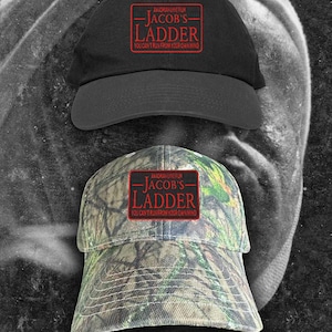 May include: Two baseball caps featuring a rectangular patch with the red text AN ADRIAN LYNE FILM JACOB'S LADDER YOU CAN'T RUN FROM YOUR OWN MIND. One cap is solid black, and the other features a green, brown, and tan camouflage pattern.