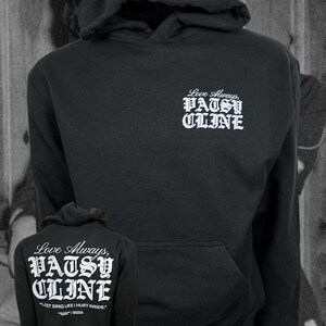 Può includere: Una felpa con cappuccio nera con testo bianco sul petto a sinistra che recita Love Always, PATSY CLINE. Il retro della felpa mostra lo stesso testo in dimensioni maggiori con la citazione I JUST SING LIKE I HURT INSIDE stampata sotto.