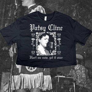 Peut inclure: Un t-shirt noir court avec une impression graphique blanche de Patsy Cline chantant dans un microphone, encadrée par des roses et des cœurs. Le texte indique Patsy Cline au-dessus et Hurt me now, get it over en dessous en police gothique.