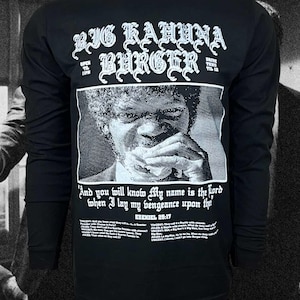 May include: A black long-sleeve shirt featuring a white graphic print. The design includes the text Big Kahuna Burger, a halftone portrait of a person eating, and the quote And you will know my name is the Lord when I lay my vengeance upon thee.