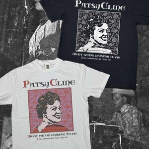 May include: Two short-sleeve crew neck t-shirts, one black and one white, each featuring a graphic of Patsy Cline. The print includes the text Patsy Cline, Night Winds Whisper To Me, and I Am Lonesome As I Can Be, set against a floral background.