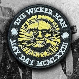 Op de afbeelding: Een ronde geborduurde patch met een zwarte achtergrond en een geel gestileerd zonnegezicht in het midden. De tekst THE WICKER MAN staat in een boog bovenaan en MAY DAY MCMLXXIII onderaan in het wit, met twee kleine witte zonne-iconen.