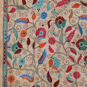 May include: A beige fabric with intricate embroidery featuring a floral pattern in shades of blue, pink, red, orange, and green. The design includes swirling vines, leaves, and flowers.
