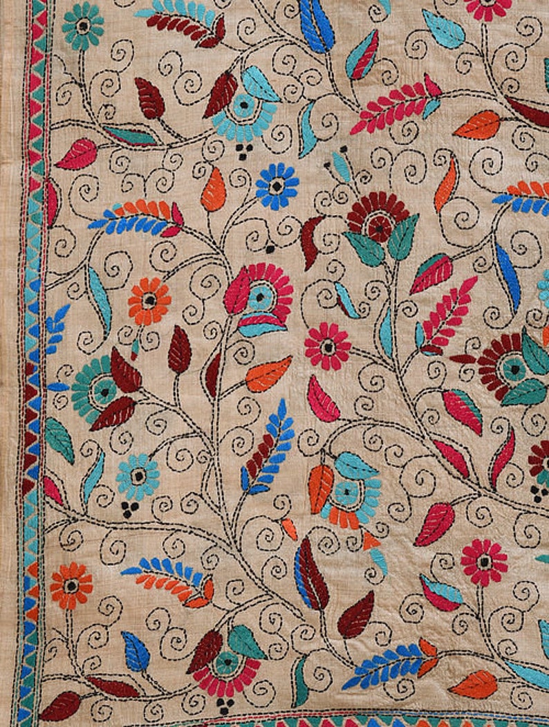 May include: A beige fabric with intricate embroidery featuring a floral pattern in shades of blue, pink, red, orange, and green. The design includes swirling vines, leaves, and flowers.