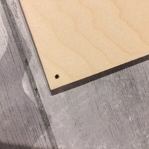 May include: A close-up of a light brown wooden board with a small black hole drilled in the center.