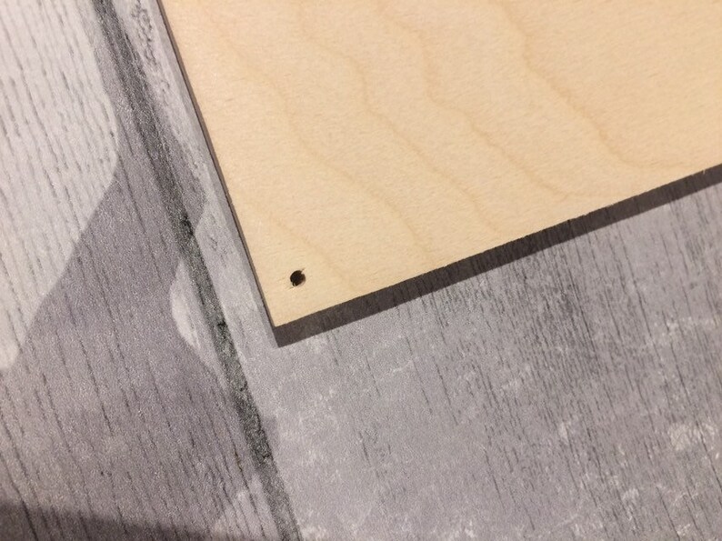 May include: A close-up of a light brown wooden board with a small black hole drilled in the center.