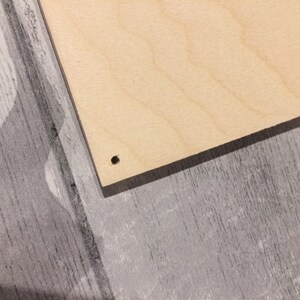 May include: A close-up of a light brown wooden board with a small hole drilled in the center.