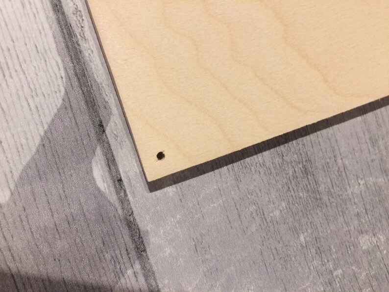 May include: A close-up of a light brown wooden board with a small hole drilled in the center.