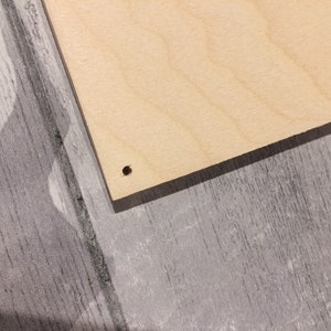 May include: A close-up of a light brown wooden board with a small hole drilled in the center.
