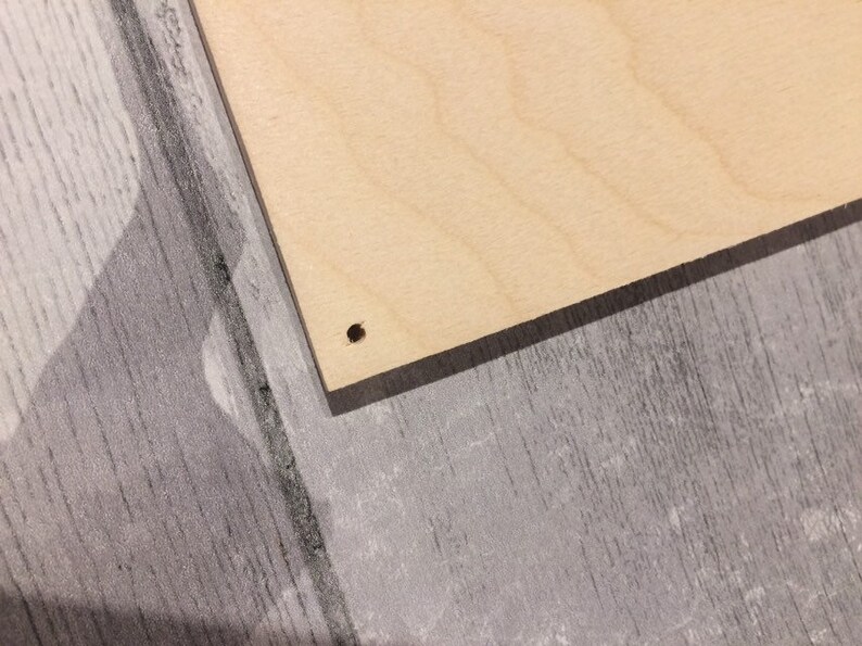 May include: A close-up of a light brown wooden board with a small hole drilled in the center.
