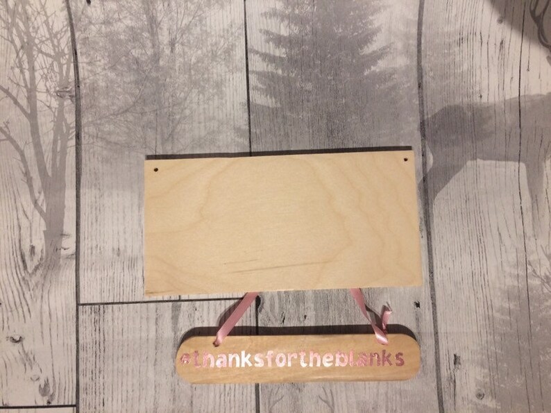 May include: A wooden sign with the text "Thanks for the blanks" in pink lettering. The sign is hanging from pink ribbon and is on a woodgrain background.