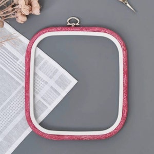 May include: A pink wooden embroidery hoop with a white inner ring and a silver metal clasp. The hoop is on a gray surface.