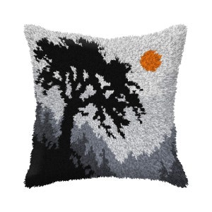 May include: A gray and black throw pillow with a silhouette of a tree and a small orange sun in the upper right corner.