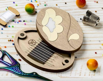 May include: Wooden oval needle case with a floral design, open to reveal needles. A pair of iridescent scissors, a thimble, and a spool of thread are also present. The scene is decorated with colorful beads and small orange spheres.