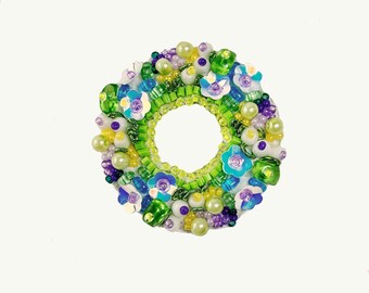 May include: A green, white, and purple beaded wreath with blue flower accents.