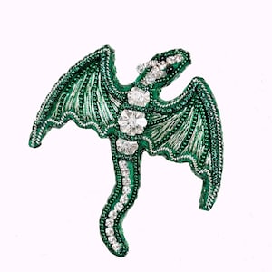 May include: A green beaded dragon with silver accents and clear rhinestone embellishments. The dragon is in a flying pose with its wings spread out.
