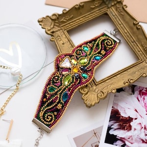 May include: A colorful beaded bracelet with a floral design and crystal accents. The bracelet is displayed in a gold picture frame.
