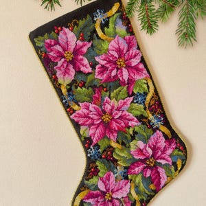 May include: A black Christmas stocking with a gold trim, embroidered with pink poinsettia flowers, green leaves, and gold ribbon.