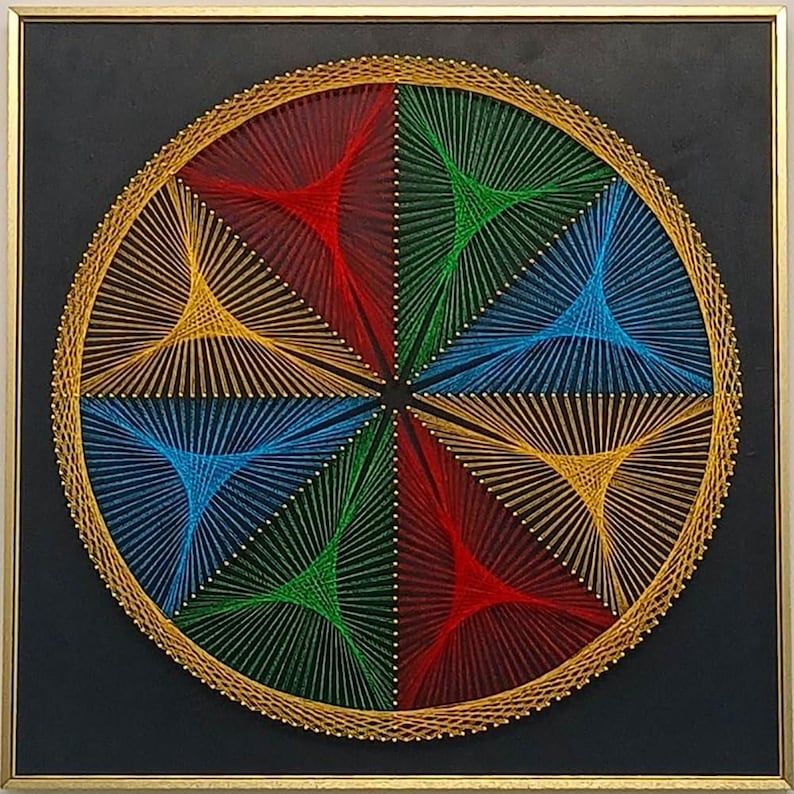May include: A square wall art piece featuring a circular string art design on a black background. The design consists of six triangular sections in red, green, and blue, created with thin threads stretched between gold pins in a gold frame.
