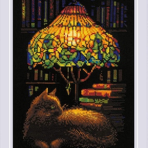 May include: Cross-stitch artwork depicting a cat resting beneath a colorful Tiffany-style lamp. The lamp's shade is a mosaic of vibrant colors, casting light on the cat and surrounding books. The background features bookshelves.