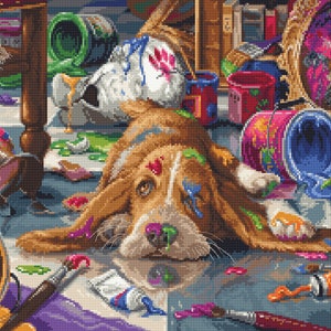 May include: A brown and white dog with paint splattered on its fur lies on a floor covered in paint.  There are paint cans, brushes, and tubes of paint scattered around the dog.