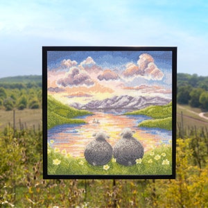 May include: A framed cross-stitch embroidery depicting a sunset over a lake with two sheep sitting in the foreground. The sky is a vibrant mix of pink, orange, and purple, with fluffy white clouds. The lake is a deep blue, reflecting the colors of the sky. The sheep are gray and white, and they are looking out at the sunset.