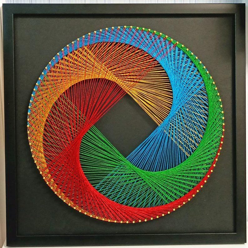 May include: A square black frame containing circular string art. The design features vibrant red, orange, yellow, blue, and green threads wrapped around gold-coloured pins, creating a geometric, swirling pattern against a solid black background.