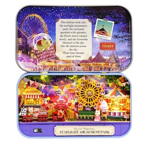 May include: A miniature amusement park diorama inside a tin. The scene includes a Ferris wheel, carousel, circus, and bakery, with the text "STARLIGHT AMUSEMENT PARK". The diorama is lit with small lights, creating a whimsical atmosphere.