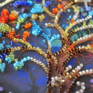 May include: Close-up of a beaded tree design. The tree trunk and branches are brown and gold, with colourful beads representing leaves in shades of blue, orange, red, and green. The background is a dark blue.
