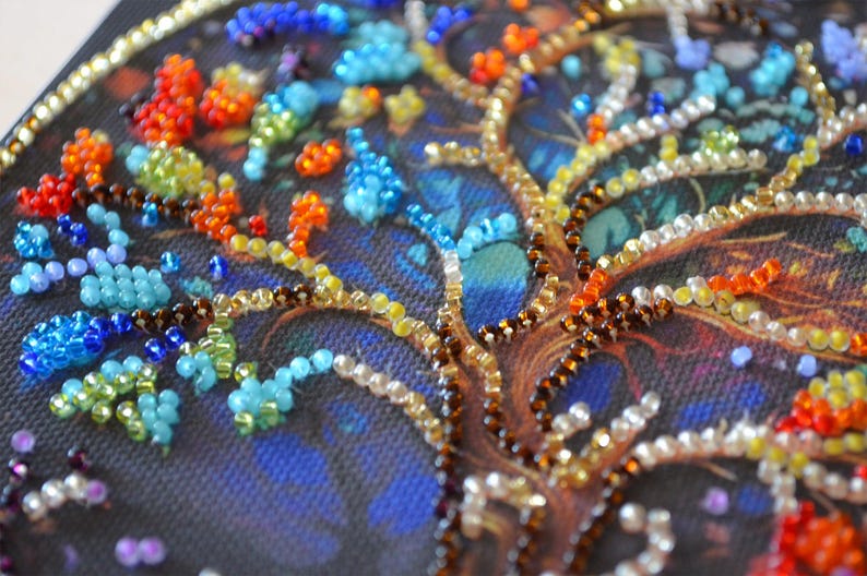 May include: Close-up of a beaded tree design. The tree trunk and branches are brown and gold, with colourful beads representing leaves in shades of blue, orange, red, and green. The background is a dark blue.