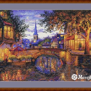 May include: A cross-stitch pattern of a quaint European town at night. The scene features a bridge over a canal, a church steeple, and buildings with lit windows. The sky is a soft purple with stars and a crescent moon. The pattern is by Merejka.