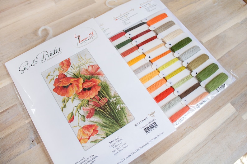 May include: A cross-stitch kit featuring a floral design of orange and red poppies. The kit includes a printed pattern, embroidery floss in various colors, and a needle. The kit is labeled "Set de Broderie" and "Luca-S".