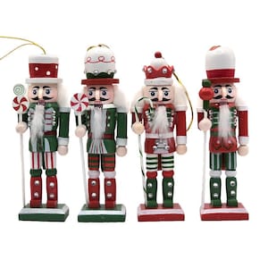 Peut inclure: Quatre casse-noisettes décoratifs en bois vêtus d'uniformes rouges, verts et blancs avec des détails peints, des barbes en fausse fourrure blanche et des cordons dorés. Chaque figurine tient un accessoire en forme de bonbon sur un socle.