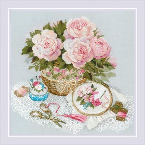May include: A cross-stitch design showing a basket of pink roses, a blue pin cushion, embroidery scissors, and a needlepoint hoop with a floral design. The scene is set on a white lace surface, with spools of thread and a pink tassel.