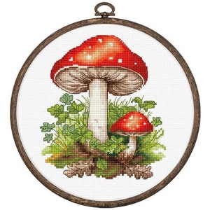 May include: Cross-stitch embroidery design featuring two red and white mushrooms with white stems surrounded by green leaves and a brown wooden frame.