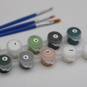 Puede incluir: Un juego de botes de pintura con los n&uacute;meros del 1 al 10, dos de los cuales est&aacute;n etiquetados como 'LAK'. Los botes est&aacute;n dispuestos en una fila sobre una superficie blanca. Hay tres pinceles en el fondo.