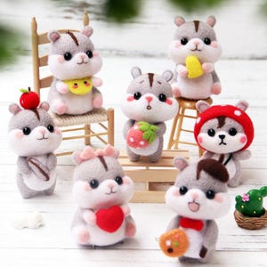 May include: A collection of adorable felted hamster figurines in various poses. Each hamster is gray and white with pink accents, some holding miniature items like a strawberry, apple, or cheese. Some hamsters are wearing accessories like a bow, bib, or hat. The figurines are displayed on a white surface.