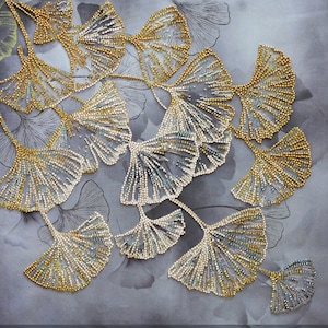 May include: A close-up of a beaded embroidery design featuring a cluster of ginkgo leaves in shades of gold and silver. The leaves are arranged in a cascading pattern, creating a delicate and intricate design.
