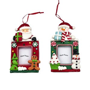 May include: Two rectangular Christmas photo frame ornaments with red ribbons. The left frame is red with Santa, a green tree, and a gingerbread man. The right frame is green with a snowman, a cupcake, and a snowman topper. Both feature candy accents.