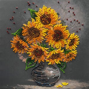 May include: A beaded artwork depicting a bouquet of sunflowers in a vase. The sunflowers are rendered in shades of yellow, orange, and brown, with green leaves. The vase is a light gray color. The background is a dark gray.