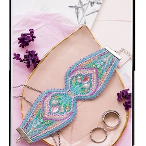 May include: A beaded bracelet kit with a light blue, pink, and green design. The kit includes 1,437 beads and measures 6.14 inches by 2.05 inches. The kit is called "Morning Tenderness" and is part of the "ABRISART" brand.