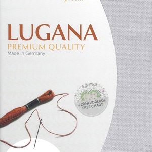 Peut inclure: Un tissu Aida blanc avec du fil &agrave; broder marron et une aiguille. Le tissu est &eacute;tiquet&eacute; "Lugana Premium Quality Made in Germany" et a les dimensions 19" x 27" (48 x 68 cm). Un cercle avec le texte "+ Z&Auml;HLVORLAGE FREE CHART" se trouve dans le coin sup&eacute;rieur droit.
