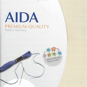 May include: Zweigart precut Aida premium quality fabric in off-white with a visible grid texture. The packaging features the text AIDA, PREMIUM QUALITY, Made in Germany, and 48 x 53 cm 19 x 21 inches. Includes a skein of blue embroidery floss.