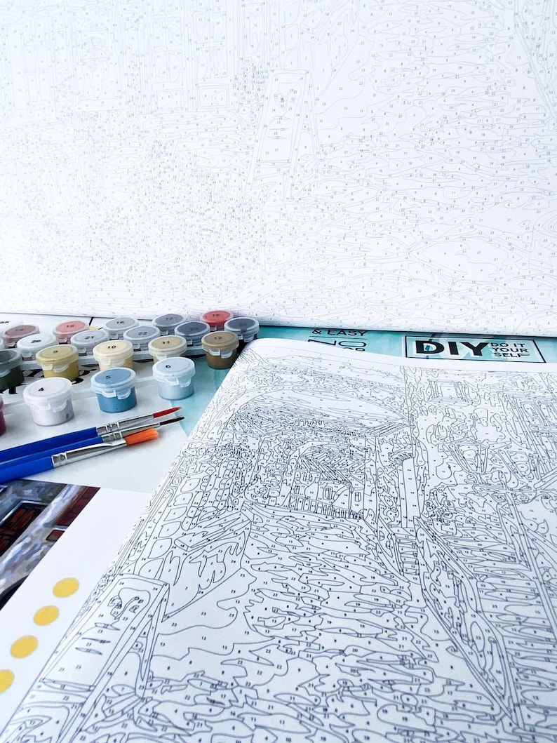 Puede incluir: Un kit de pintura por n&uacute;meros con un dise&ntilde;o de paisaje urbano. El kit incluye un lienzo, pinceles y peque&ntilde;os frascos de pintura acr&iacute;lica. El lienzo est&aacute; parcialmente rellenado con n&uacute;meros, que indican d&oacute;nde aplicar cada color de pintura. El kit tambi&eacute;n incluye el texto "DIY & EASY NO. 20" y "DO IT YOURSELF".