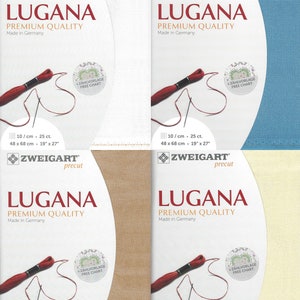 May include: Four packages of Zweigart Lugana Aida cloth, a premium quality fabric for cross stitch. The packages are white, light blue, beige, and cream. Each package has a red thread and needle, and the text "Zweigart precut Lugana Premium Quality Made in Germany" is printed on the front. The dimensions are 19" x 27" (48 x 68 cm).