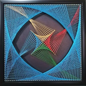 May include: A square string art piece in a black frame featuring a dark background with geometric patterns created by taut threads in shades of blue, red, green, and gold. The threads are anchored by small silver pins forming a circular design.