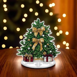 May include: A green Christmas tree with gold bows and white beads, standing on a white base with two red and white gift boxes. The tree is illuminated from below.