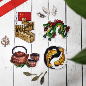 May include: Four cross-stitch embroidery designs featuring Chinese cultural symbols: the Great Wall of China, a dragon, a yin-yang symbol with fish, and a teapot and teacups.