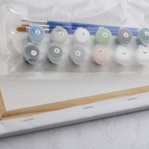 Puede incluir: Un kit de pintura por n&uacute;meros que incluye un lienzo, pinceles y 10 peque&ntilde;os frascos de pintura acr&iacute;lica. Los frascos de pintura est&aacute;n etiquetados con los n&uacute;meros del 1 al 10, y el lienzo es parcialmente visible en el fondo.